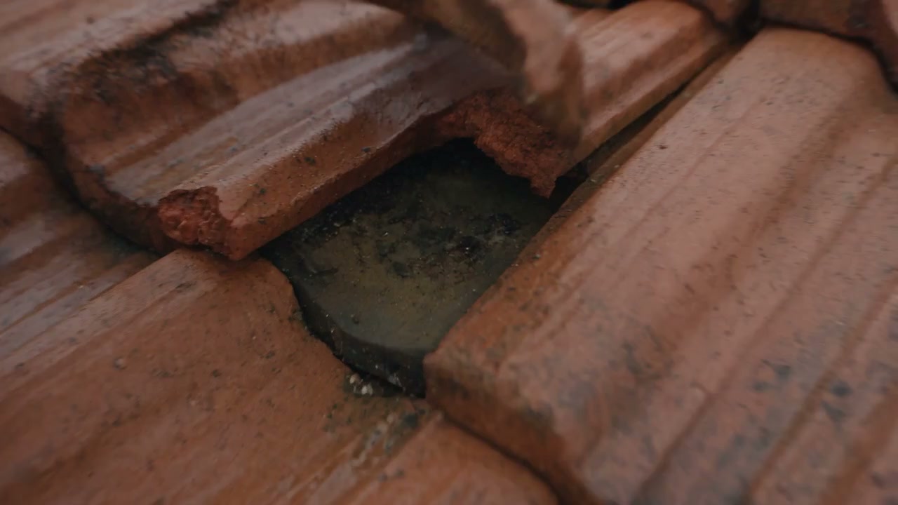 A lifted terracotta roof tile showing the gap water actually gets in through, from the film