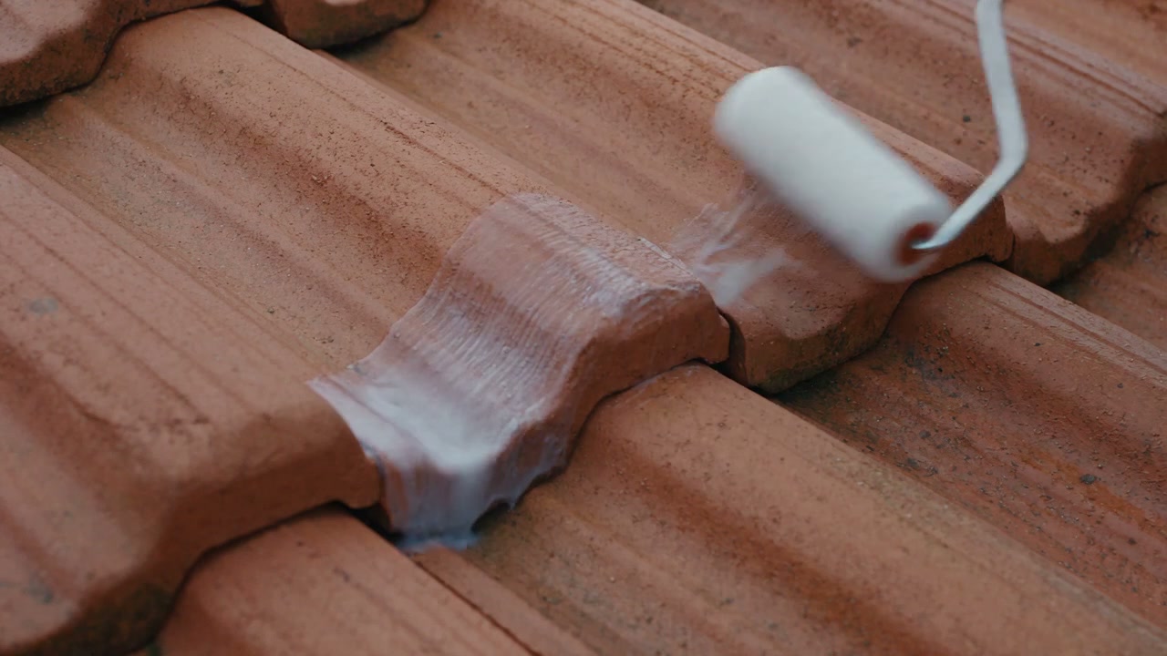 Flexible waterproof compound being rolled along a join in a tiled roof, from the film
